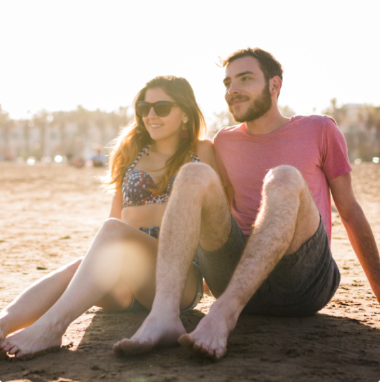 Imagem de um homem e uma mulher sentados na areia de uma praia