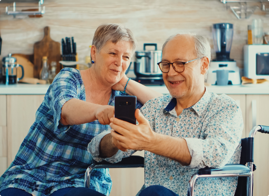 Imagem de um senhor e uma senhora dentro de casa mexendo no celular